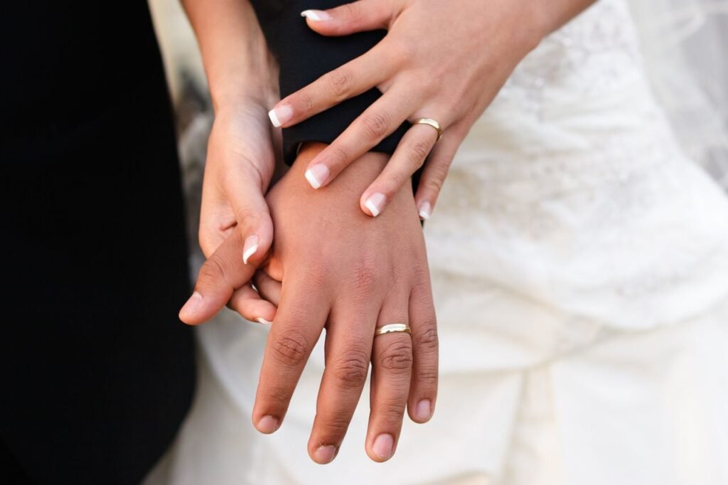 A bride and groom touching hands with wedding bands prominently displayed during a ceremony.